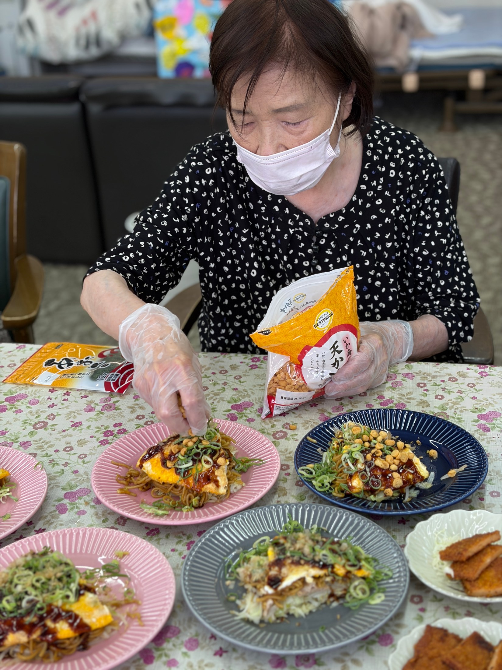 利用者さんがお好み焼きに天かすとねぎをトッピングしている様子