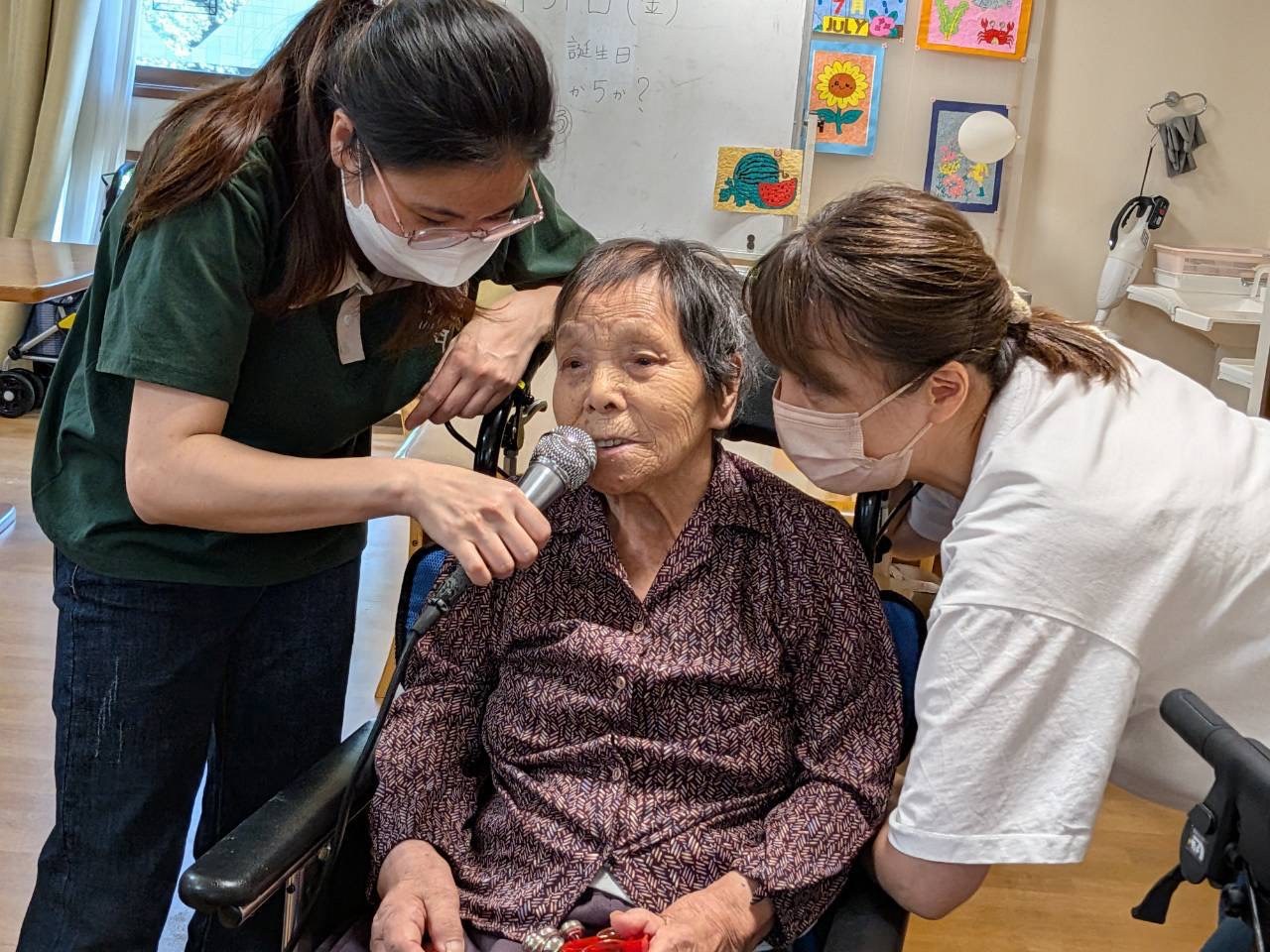 マイクを手に歌う98歳のH様を職員がそばで応援するカラオケの様子