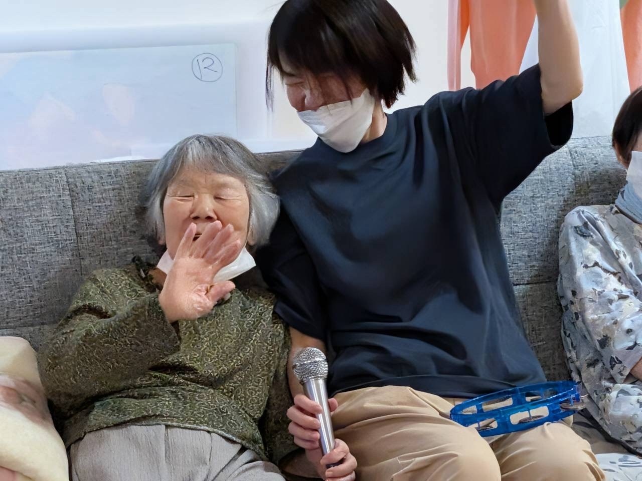 カラオケで手を振る利用者さんとタンバリンを持って盛り上がる職員