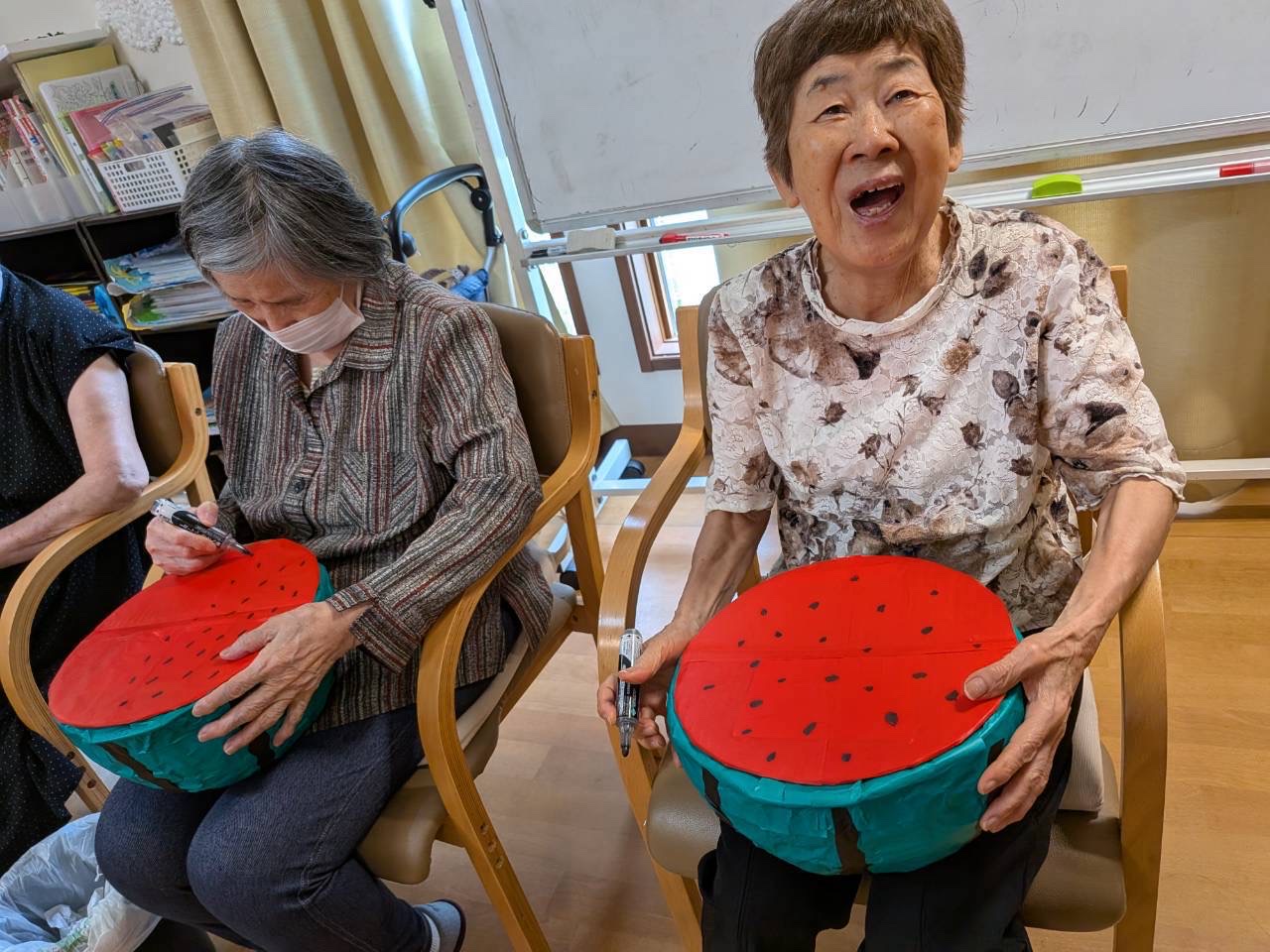 大きなスイカの工作を手に、種を描き加えている利用者さんたち