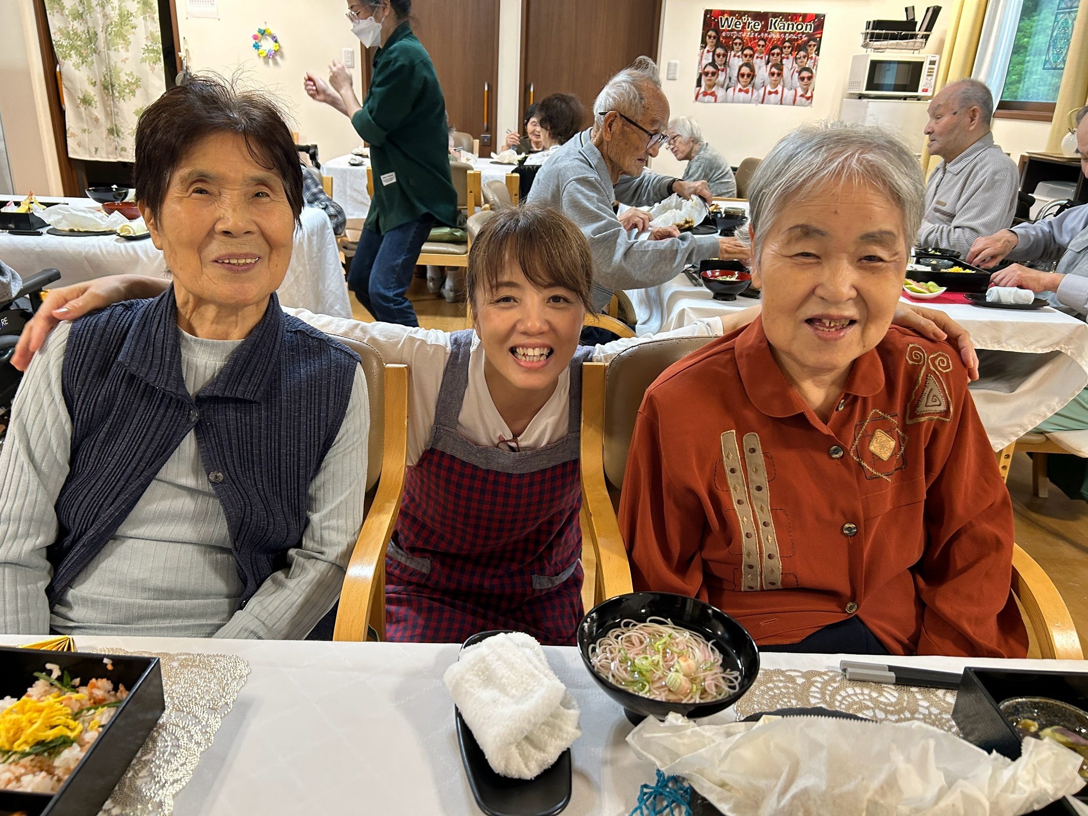 食卓で利用者さんおふたりと職員が笑顔で並ぶ様子