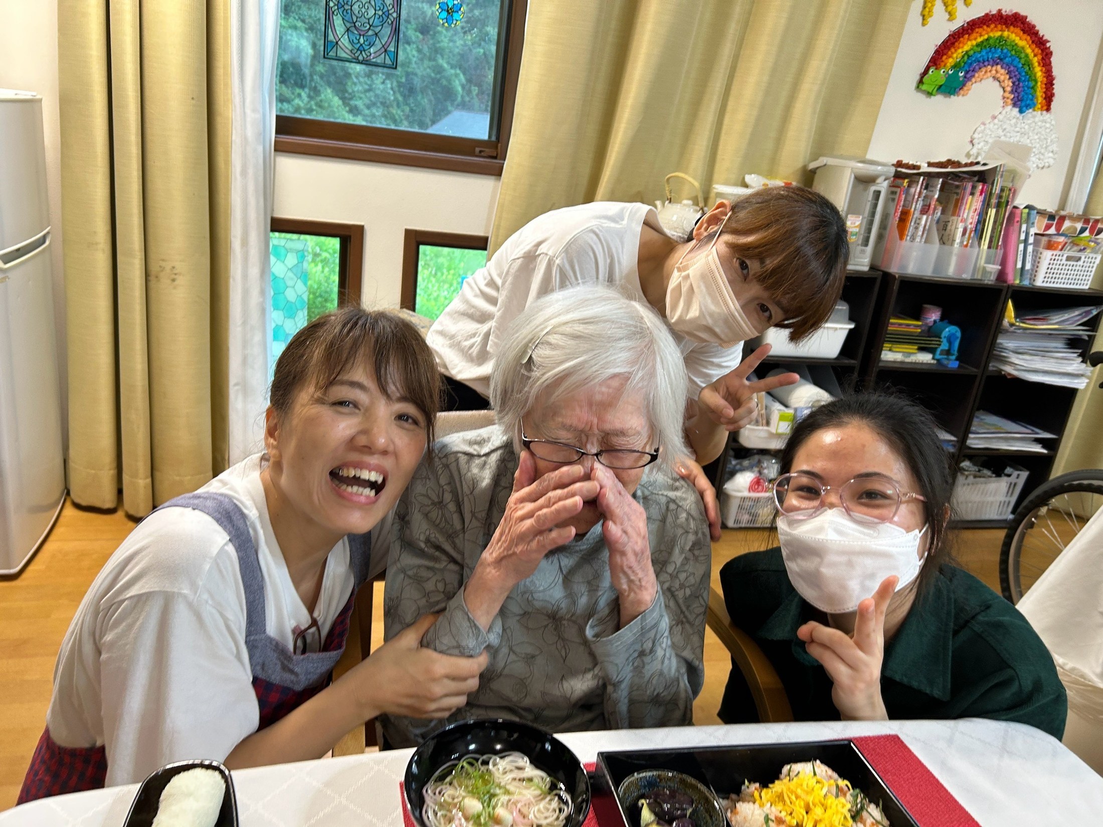 食卓で利用者さんに寄り添い職員が記念撮影する様子