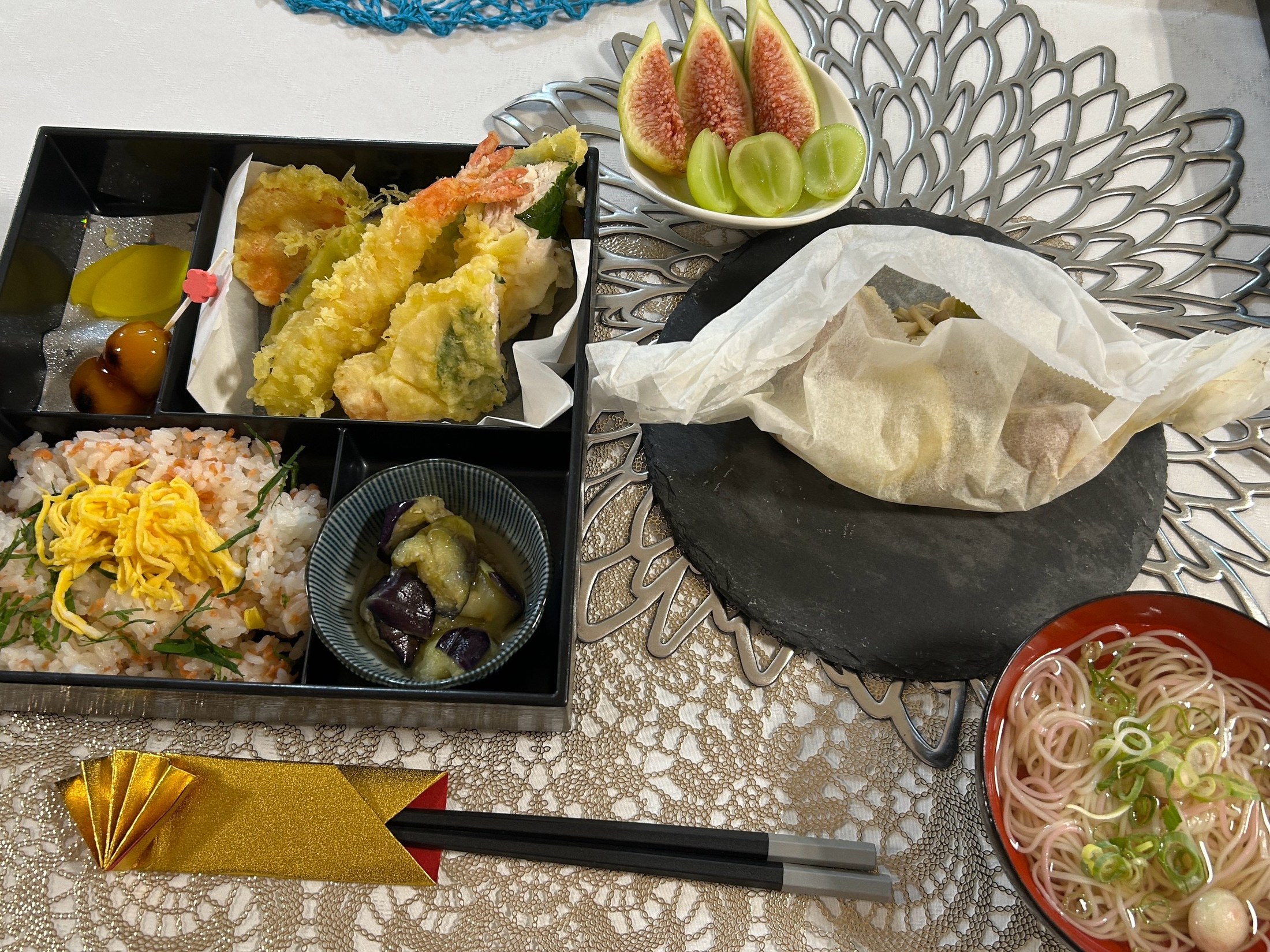 ちらし寿司、天ぷら、麺、いちじくとぶどうが並ぶ食事