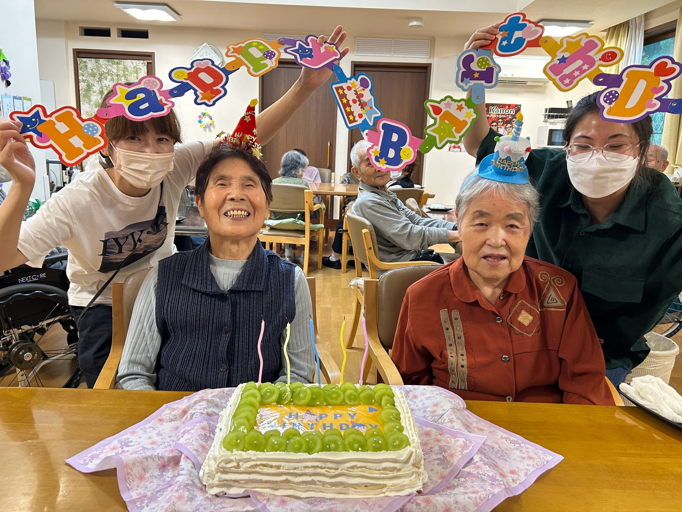 ぶどうのケーキを前に利用者さんおふたりと職員がお祝いする様子