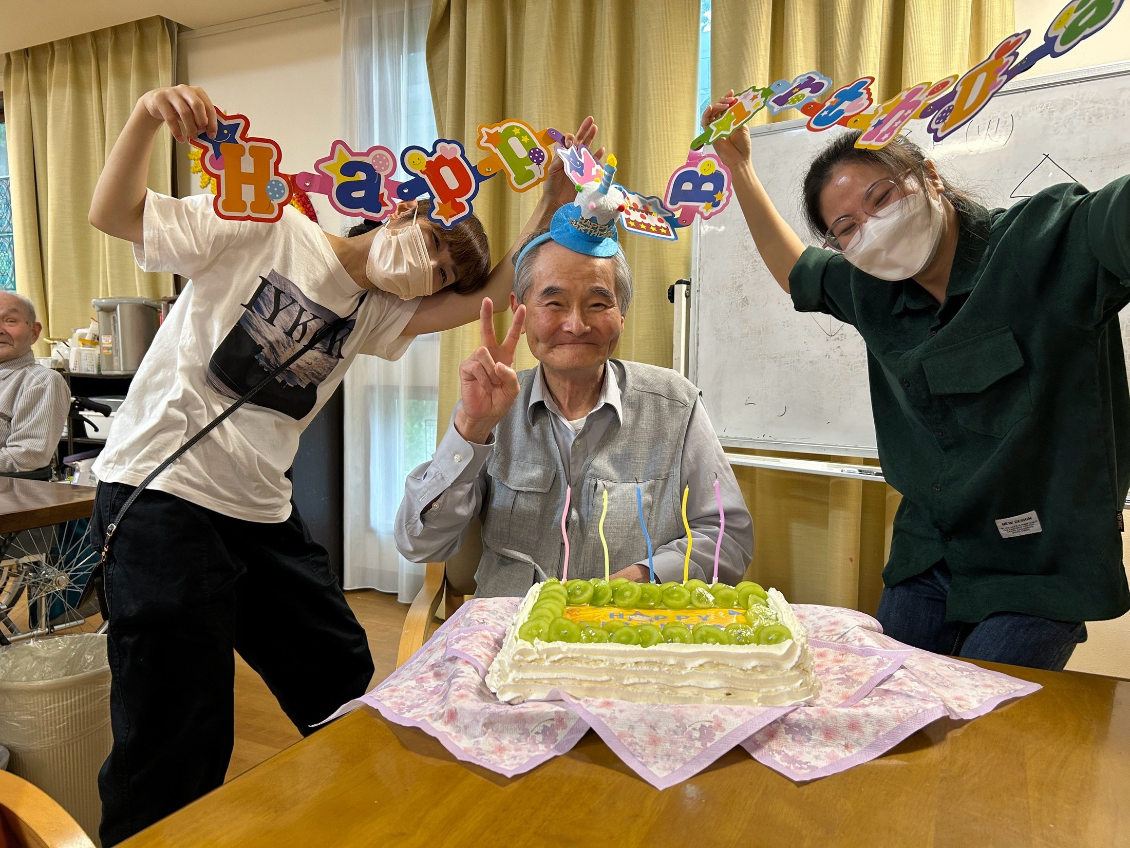 誕生日の帽子をかぶりケーキの前でピースをする利用者さん