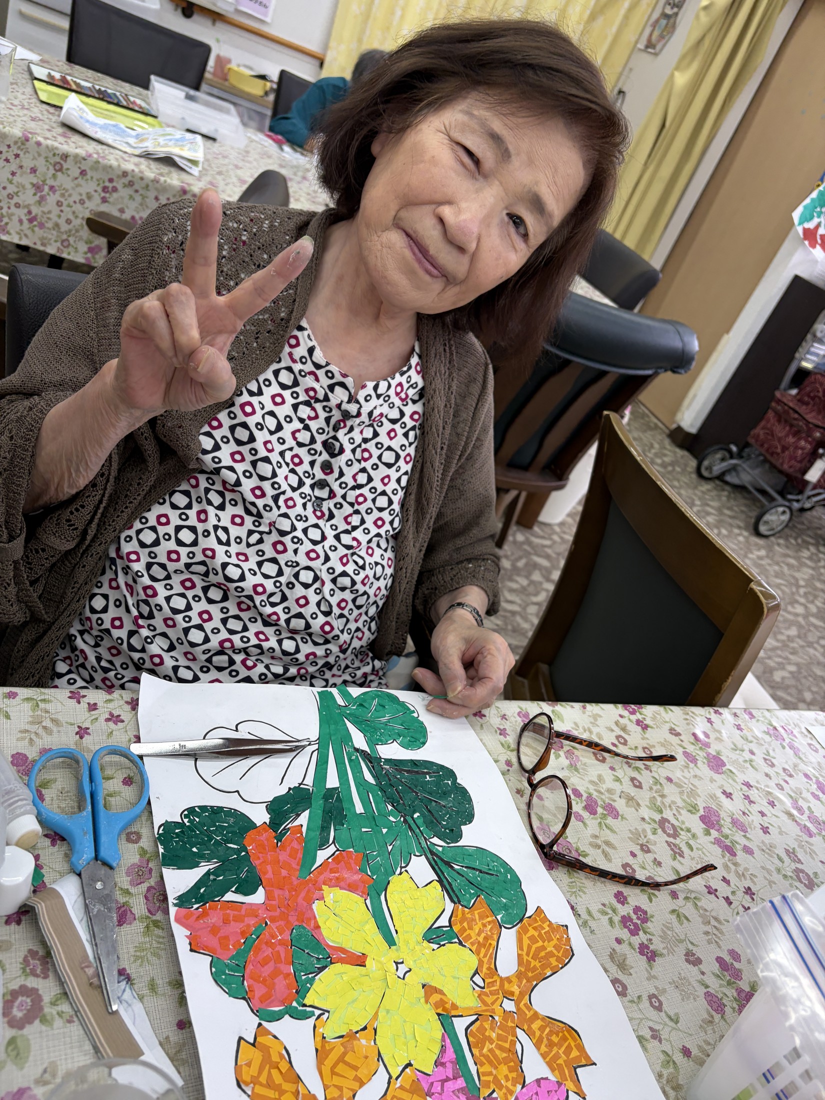花の貼り絵を前に笑顔でピースをする利用者さん