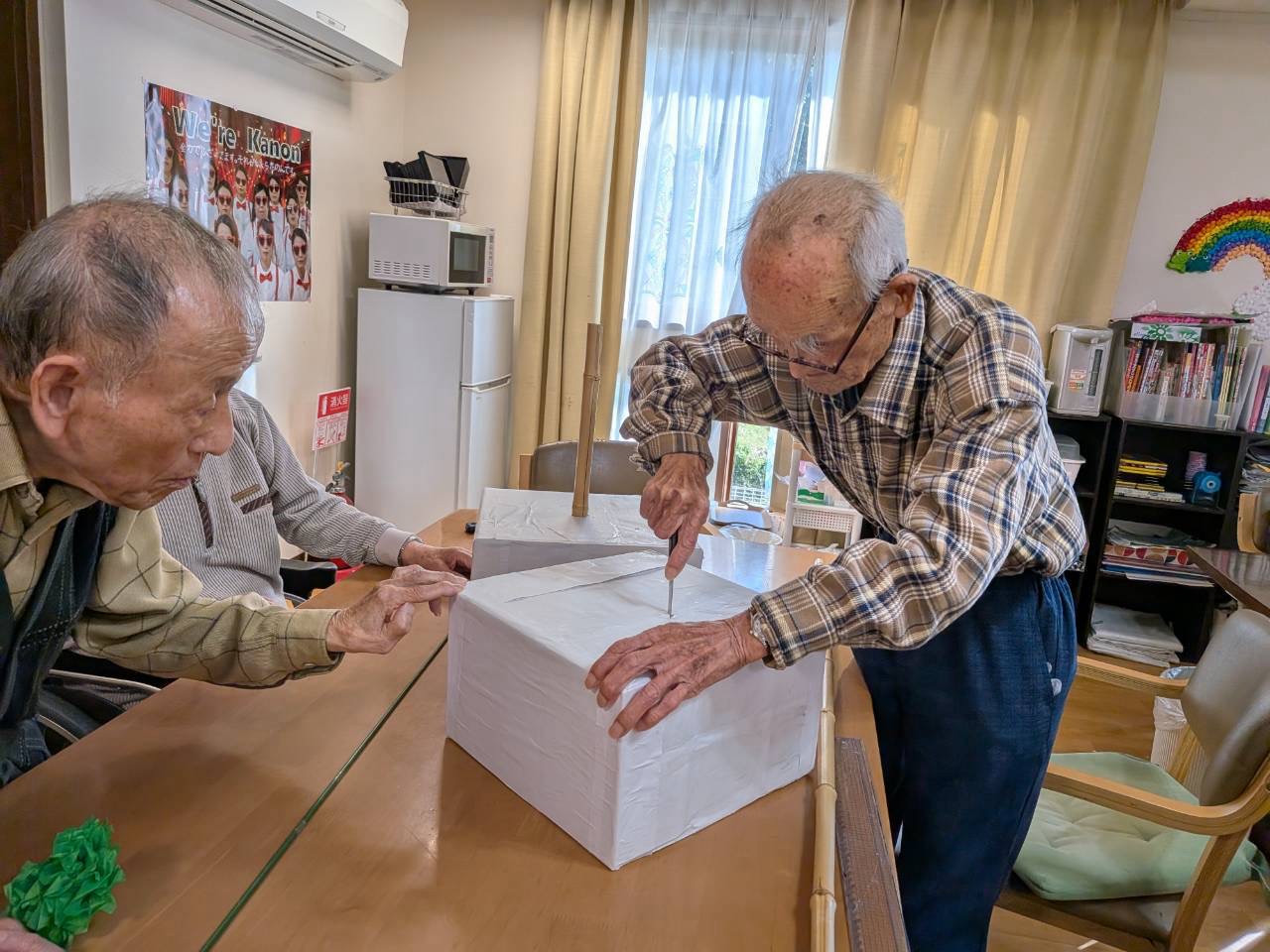 白い紙で覆った箱を支えながら道具で作業をするおふたり