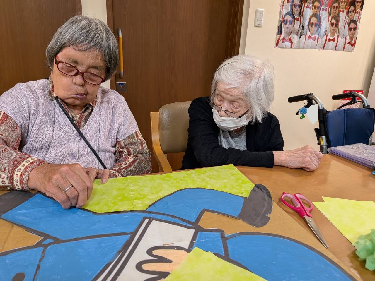 青と黄緑の大きな作品に手を添えて制作するおふたり