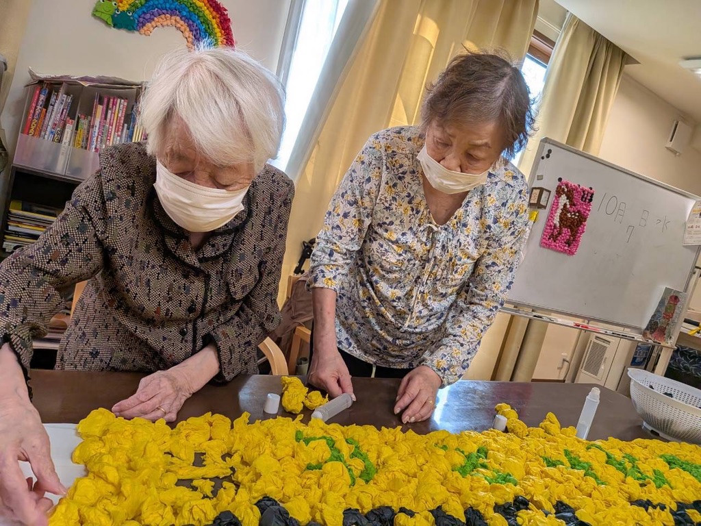 丸めた黄色いお花紙で顔はめパネルの下に置く看板を作るおふたり