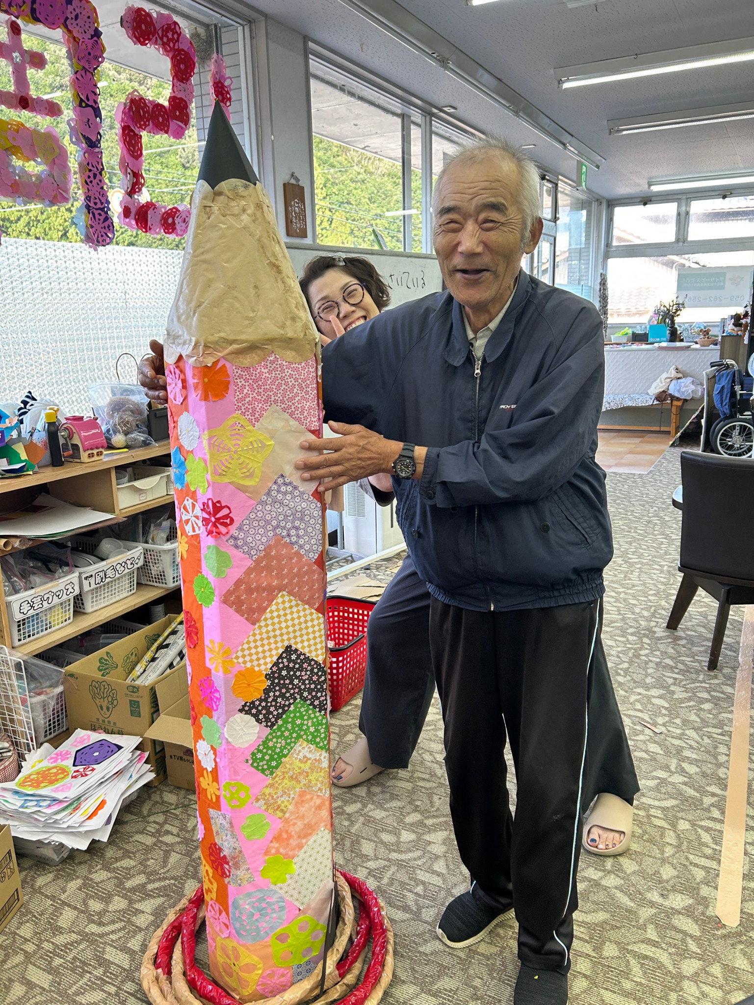 色とりどりの紙や花の飾りを貼った巨大鉛筆を支える利用者さんと職員