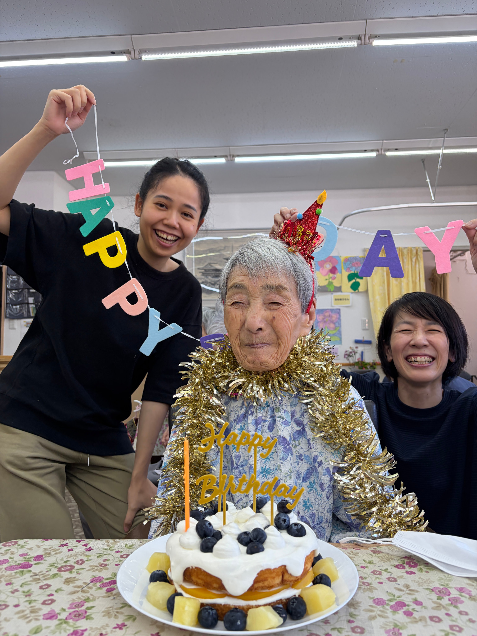 誕生日の飾りを身につけ、ケーキを前に職員と記念写真に写るS様