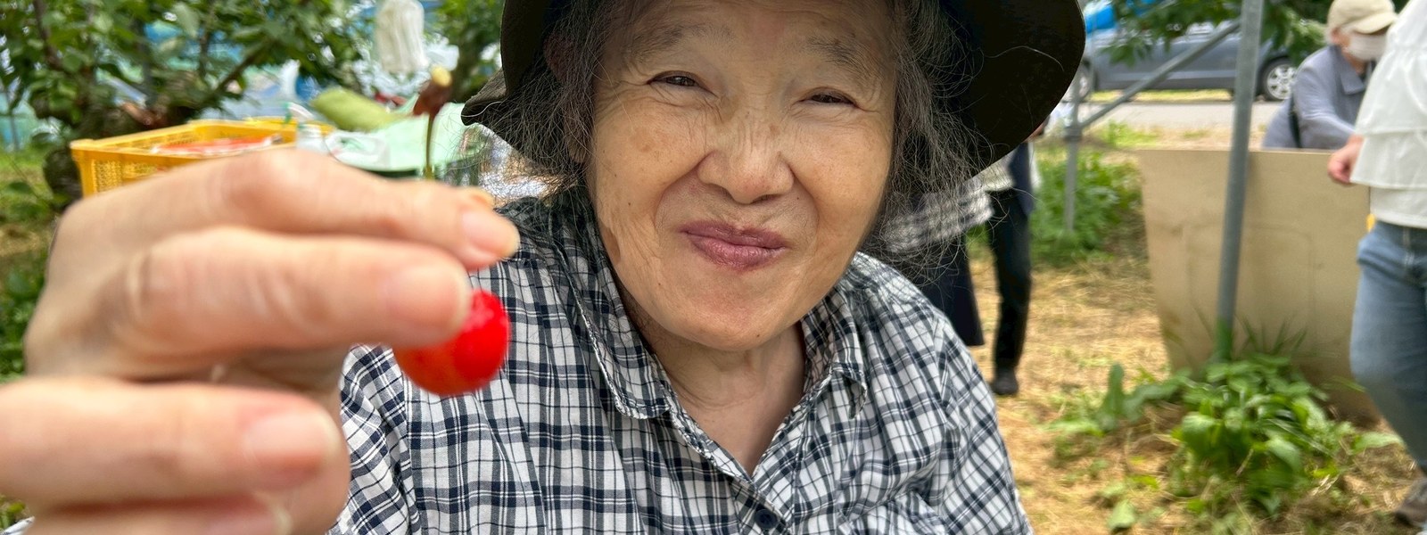 屋外でさくらんぼを手に笑顔を見せる利用者さん