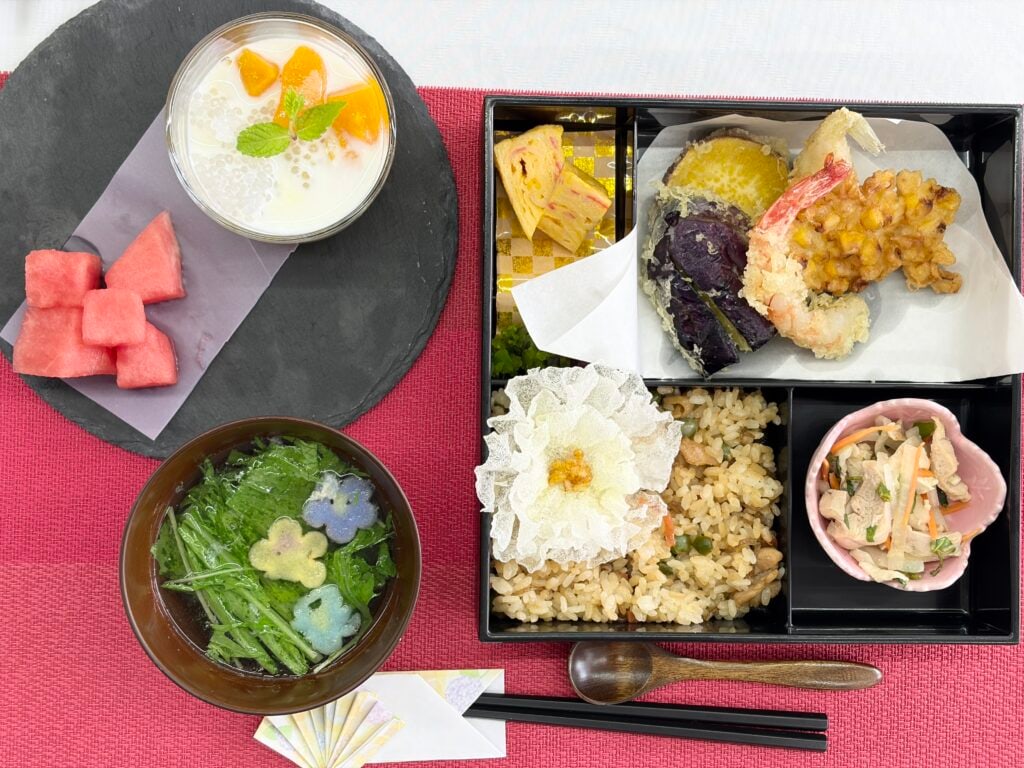 炊き込みご飯や天ぷら、すいか、ミルクデザートが並んだお祝いのお弁当